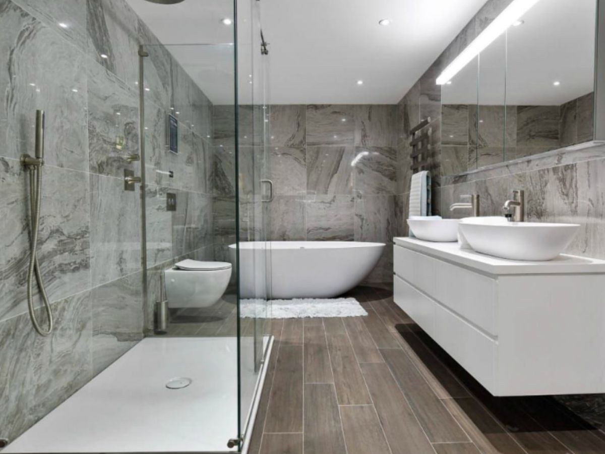 Salle de bain marbre gris, baignoire îlot blanche, double vasque et douche vitrée.