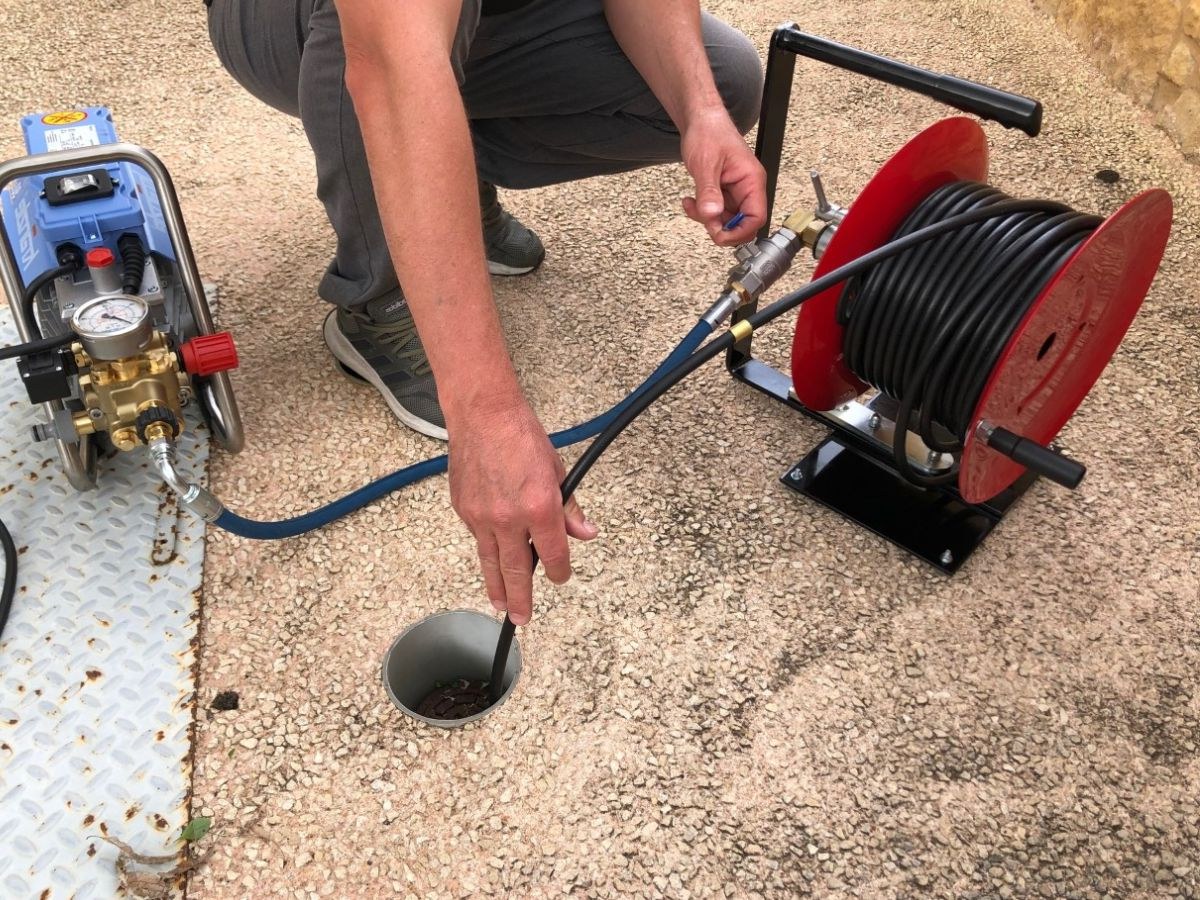 Personne accroupie poussant un flexible noir dans un regard, pompe bleue et enrouleur rouge à côté.