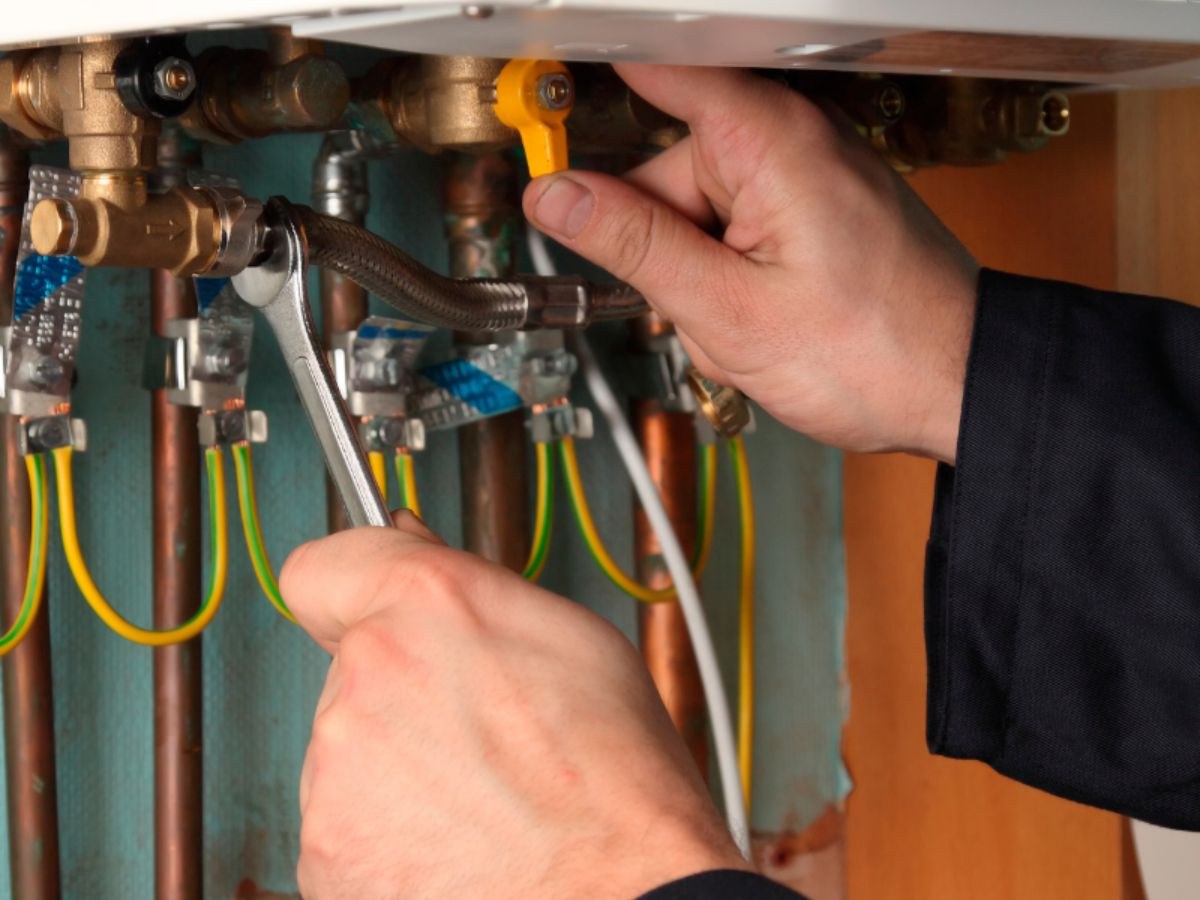 Mains sur une vanne jaune et une clé plate, flexible tressé et colliers de terre sur du cuivre.