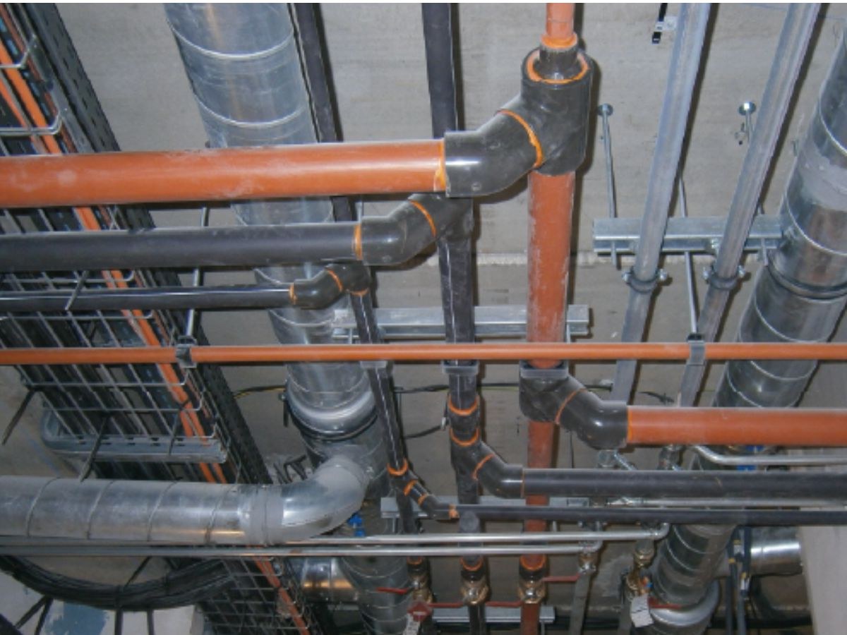 Tubes PVC orange et gaines métalliques annelées fixés sous un plafond béton par des tiges filetées.