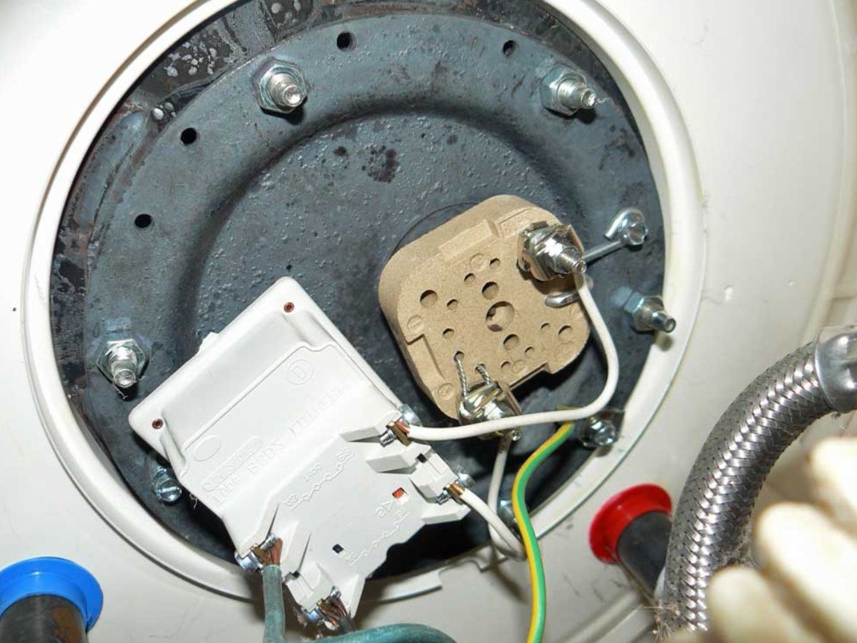 Dessous d'un chauffe-eau : thermostat, tête de résistance céramique, fils blancs et flexible inox.