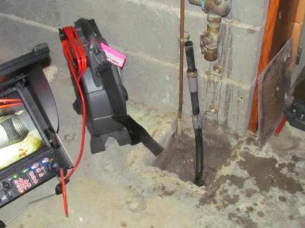 Console d'inspection, écran de canalisation, enrouleur de câble rouge et sonde dans une ouverture au sol.