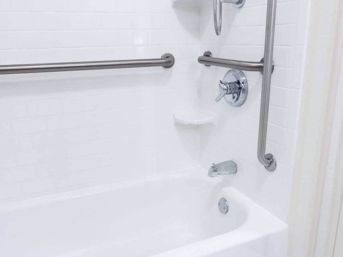 Baignoire blanche, bec chromé et deux barres d'appui, carrelage métro et tablette d'angle.
