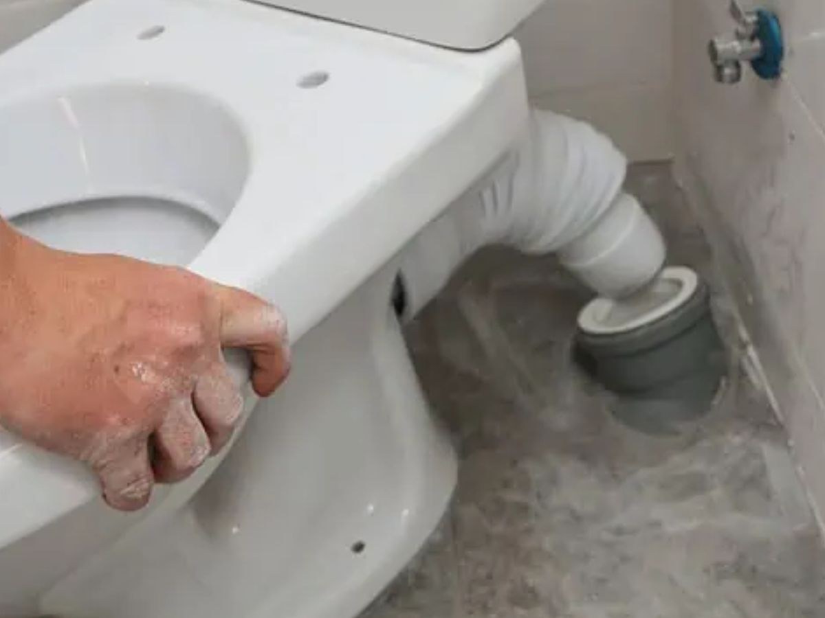 Main posant une cuvette blanche, pipe souple accordéon branchée vers l'évacuation PVC au sol.