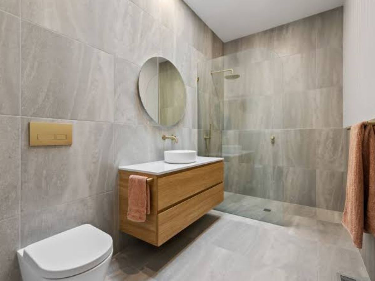 Salle de bain gris pierre, meuble chêne suspendu, vasque ronde et robinetterie dorée.