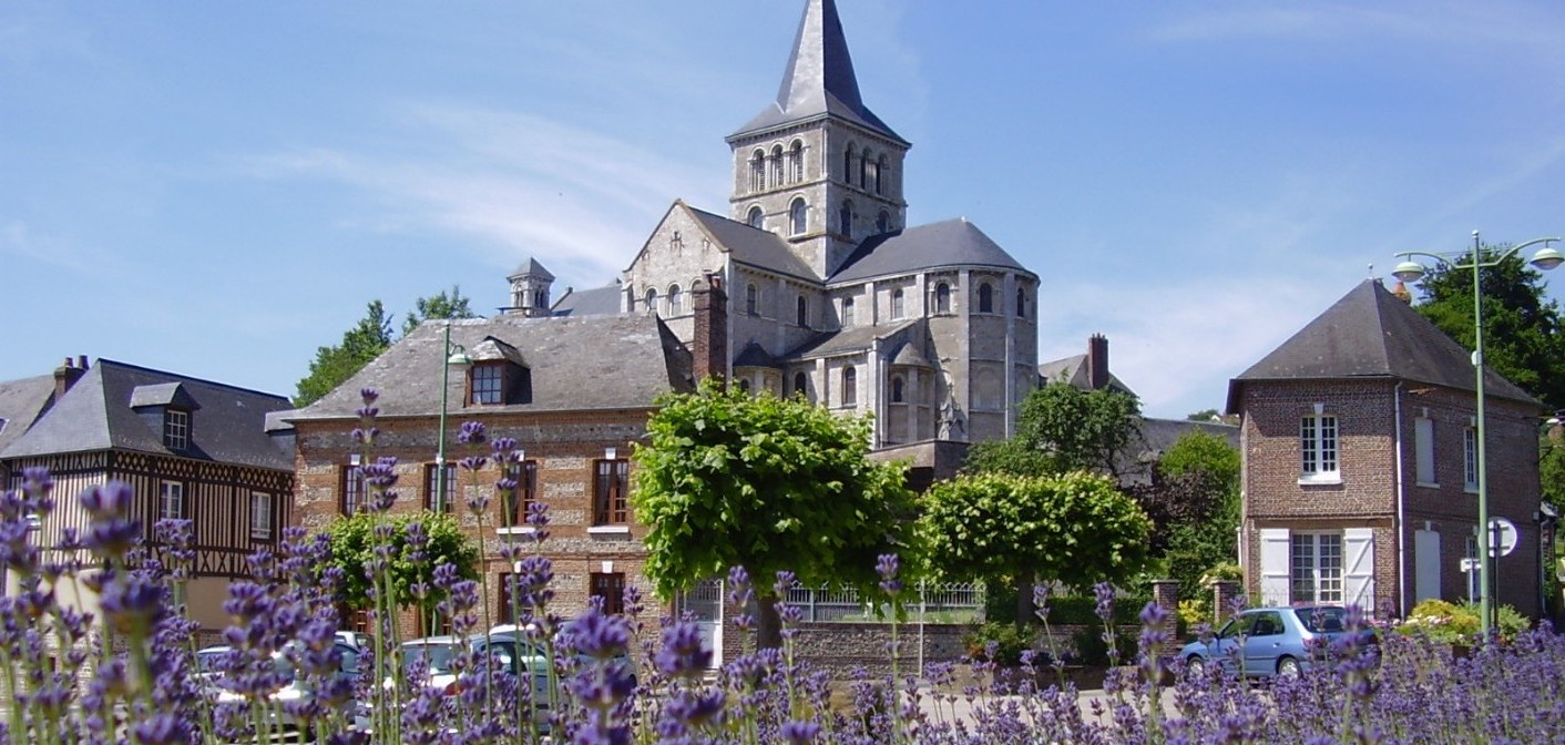 Église en pierre à flèche sombre, maisons à colombages et massif de lavande violette au premier plan.